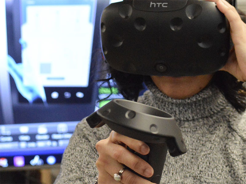An undergraduate student wears a VR headset and uses a joystick.